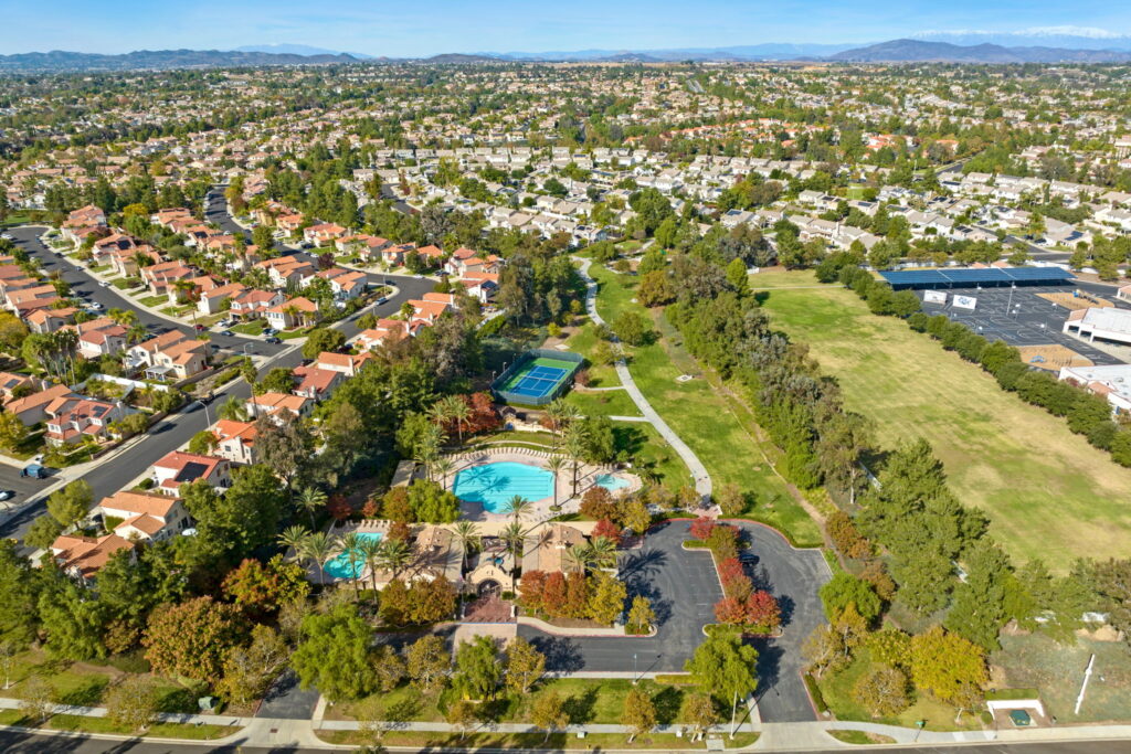 Aerial view of a residential neighborhood in Temecula, California, featuring community amenities like pools, tennis courts, parks, and nearby schools with mountain views in the distance.